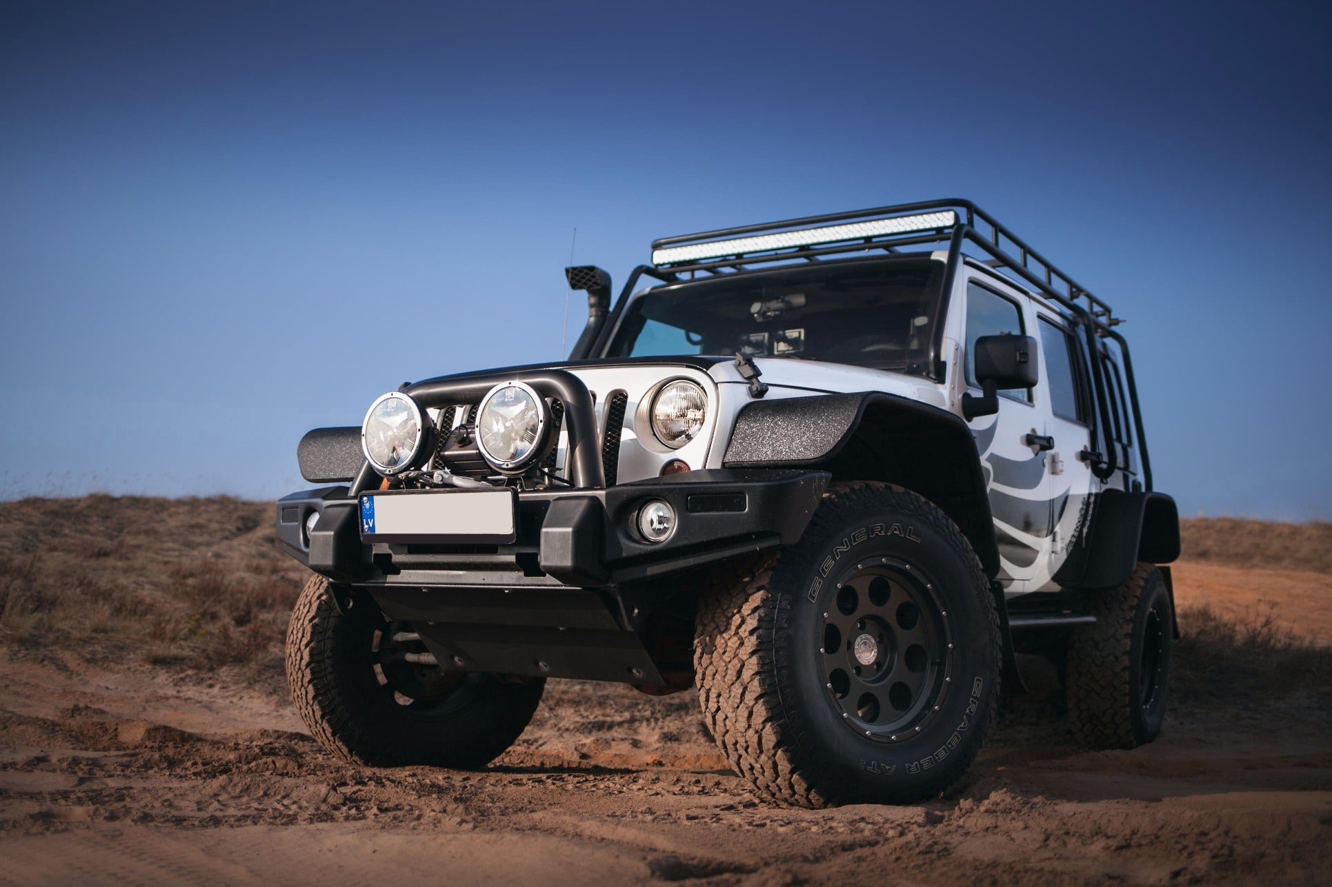 Off-road vehicle with black and white exterior, large tires, front bumper, and LED light bar on a dirt trail.
