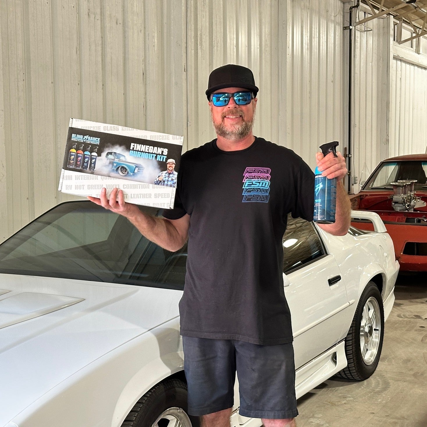 Mike Finnegan holds the Burnout Kit in front of a white car, showcasing automotive products for car enthusiasts.