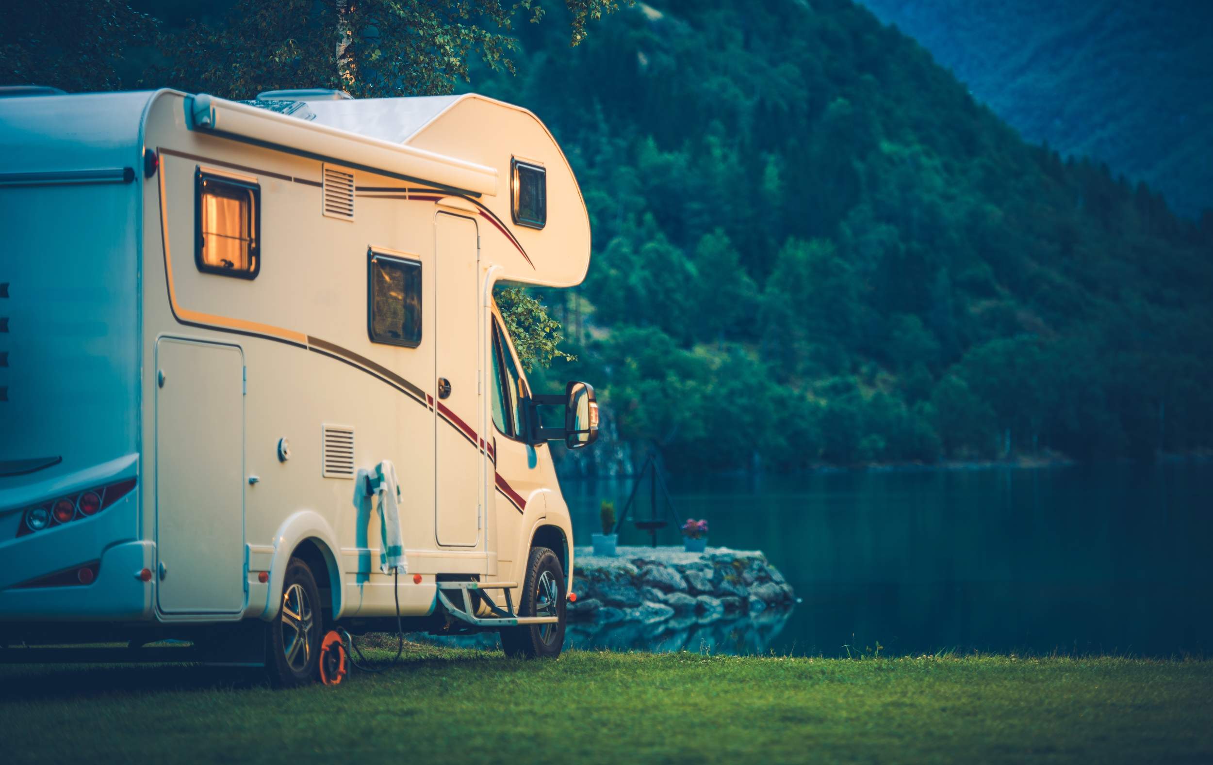 RV parked by a lake with lush green mountains in the background, emphasizing premium vehicle cleaning and detailing products.