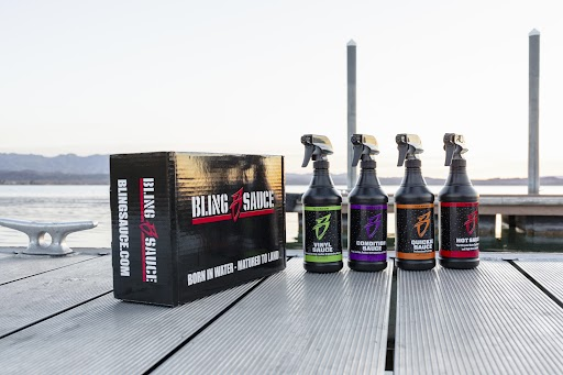Bling Sauce 4-Pack Kit displayed on a dock, featuring four spray bottles and a branded box against a scenic water backdrop.