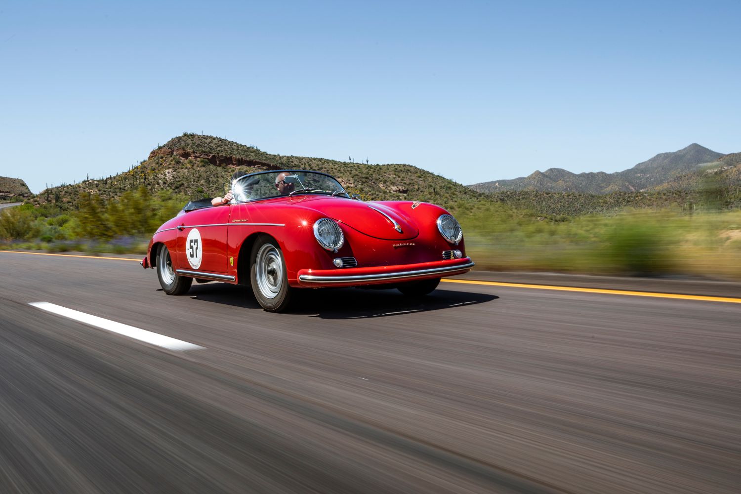 Red vintage Porsche convertible driving on a highway, showcasing sleek, shiny car details and vibrant color.