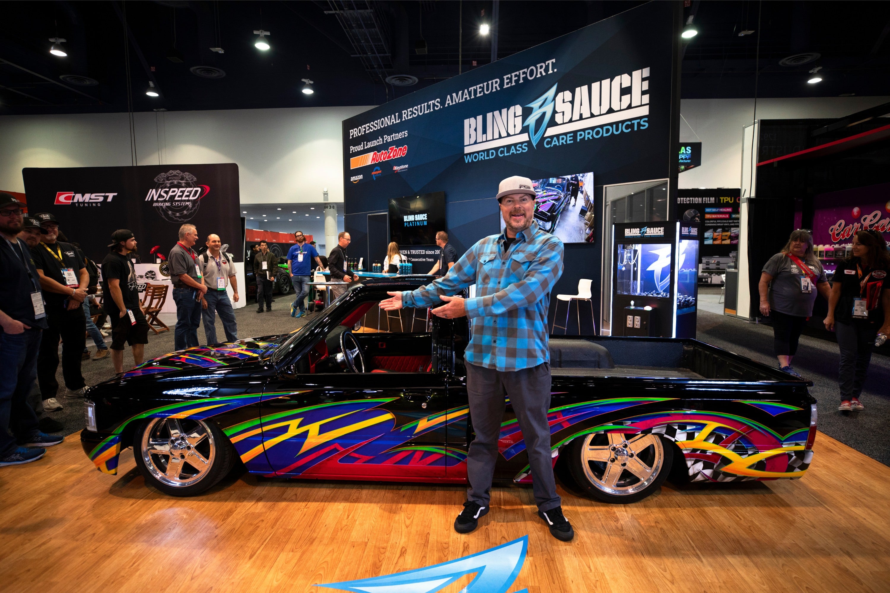 Man pointing at a custom black vehicle with colorful graphics, at a car care product expo booth with branding for Bling Sa...