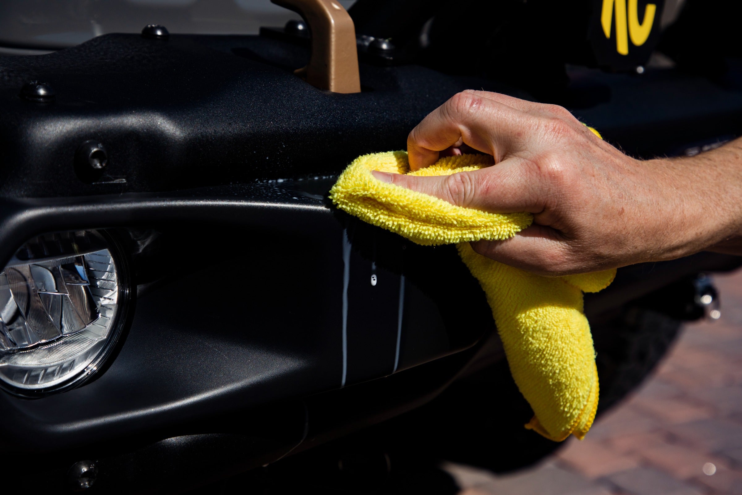 Hand wiping a black vehicle with a yellow microfiber cloth, focusing on premium car detailing for professional results.