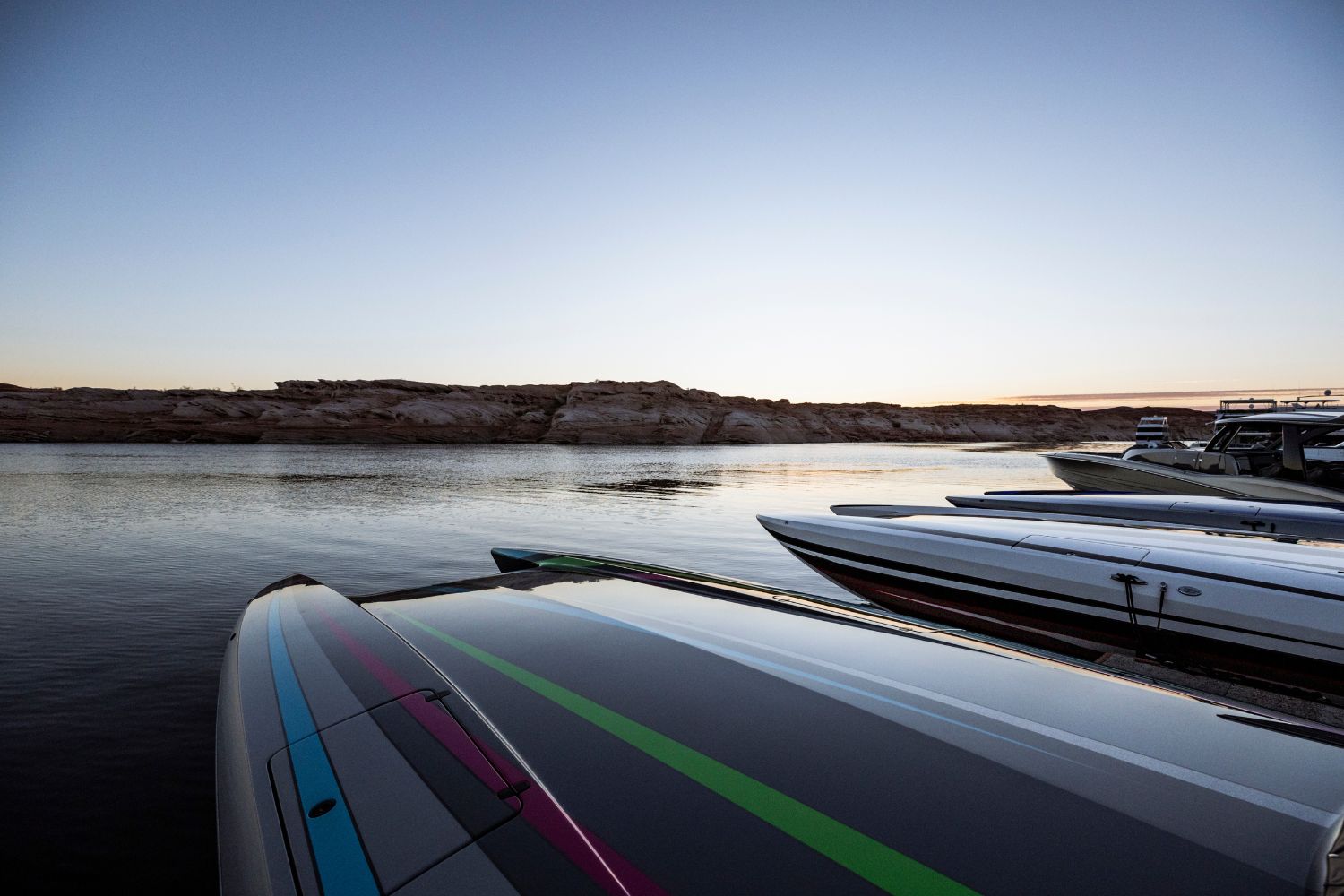 Multiple luxury boats docked on calm water at sunset, showcasing sleek designs and vibrant, colorful accents.
