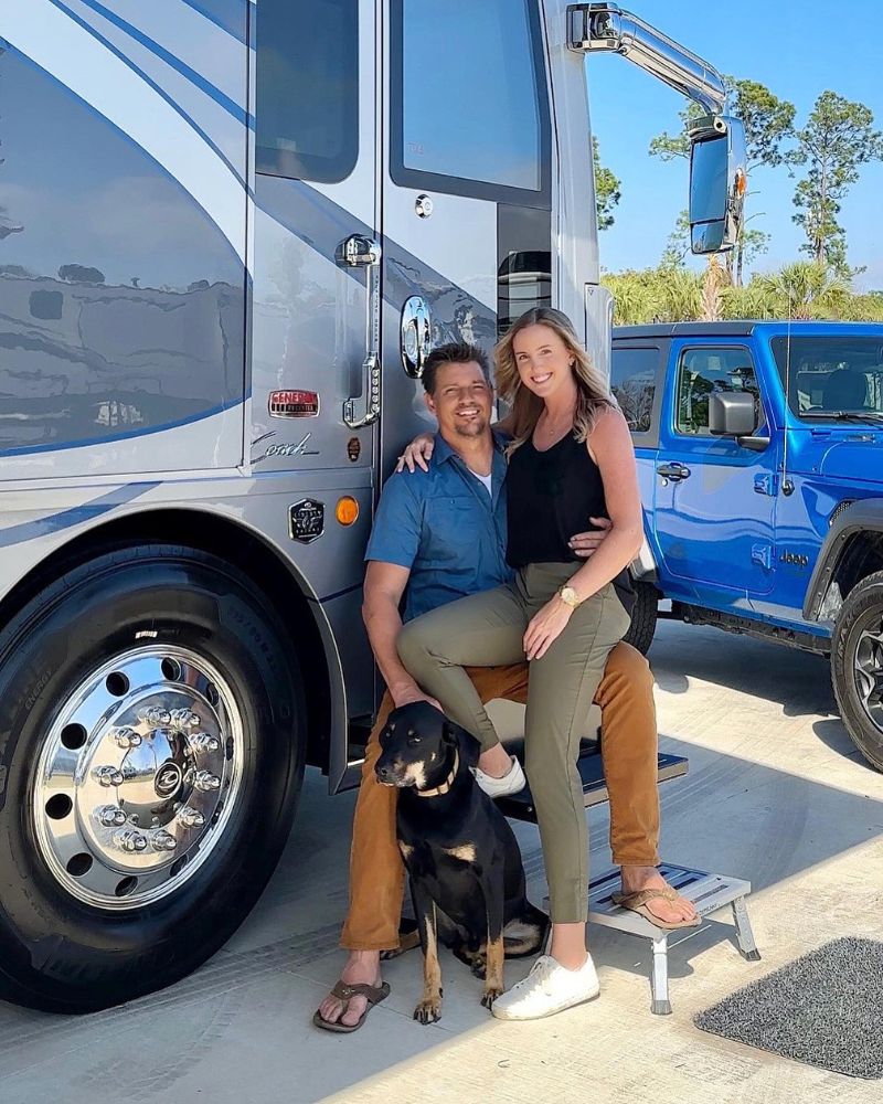 Happy couple with dog in front of a shiny, blue and silver RV and truck, showcasing premium vehicle cleaning products for ...
