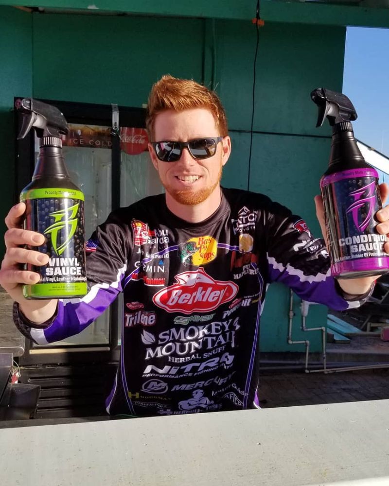 Man holding two black spray bottles with colorful labels, one green and one purple, for vehicle cleaning and detailing.