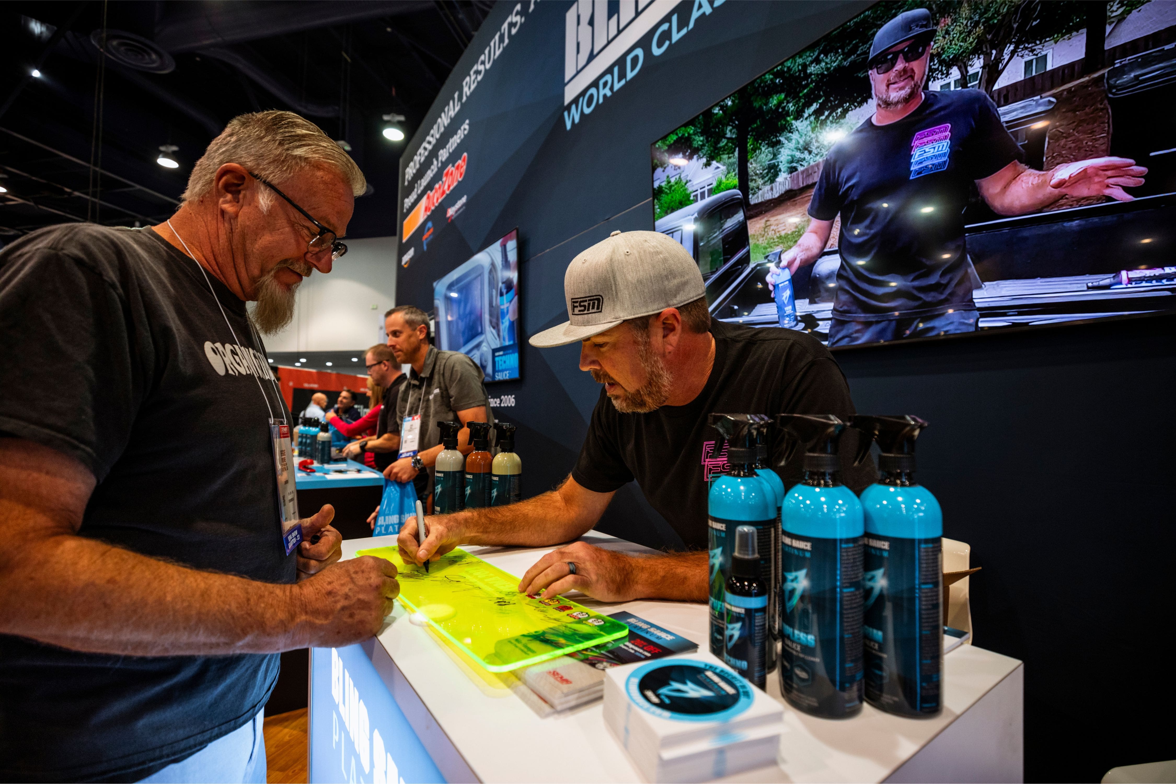 Display of premium vehicle detailing products at a trade show, featuring blue spray bottles, black spray nozzles, and vibr...